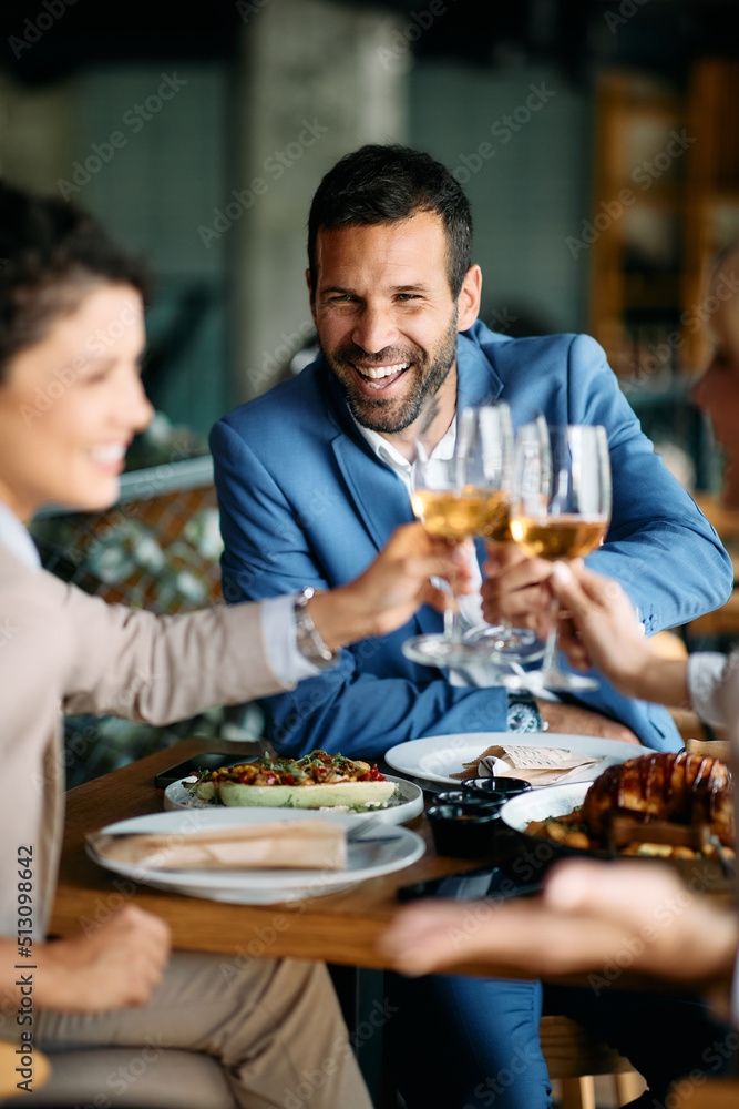 Happy businessman and his colleagues toasting with wine while having lunch in restaurant.