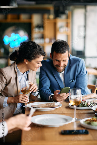 Happy business couple using smart phone during lunch in restaurant.