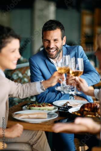 Happy businessman and his colleagues toasting with wine while having lunch in restaurant.