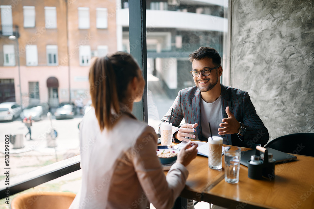 Happy businessman talks with female colleague during breakfast in cafe.