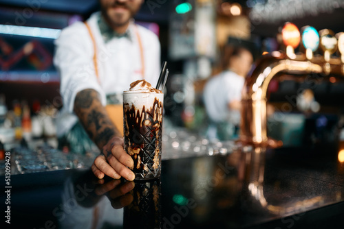 Close up of barista serving iced coffee in tall glass at bar counter.