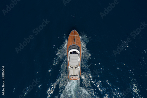 Luxurious wooden boat fast movement on dark water..Classic Italian wooden boat fast moving aerial view. Top view of a wooden powerful motor boat with an awning. © Berg