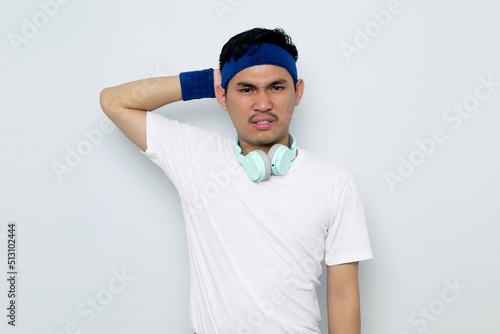 Portrait of pensive young Asian sportman in blue headband and sportswear white t-shirt with headphones, wonder about question isolated on white background. Workout sport concept photo