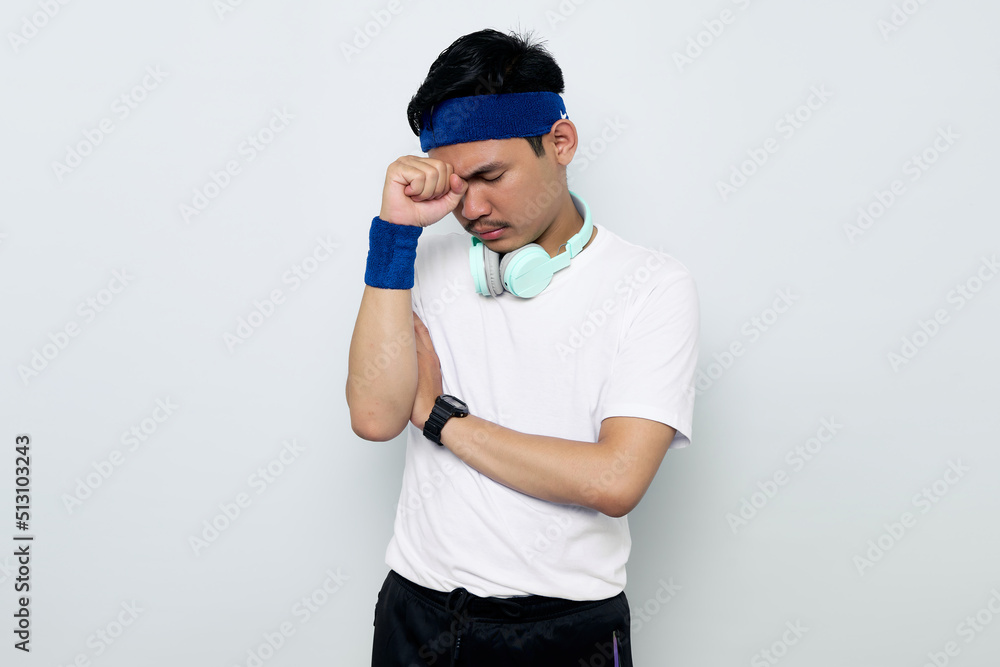 Depressed young Asian sportman in blue headband and sportswear white t-shirt with headphones, Having Problems And Suffering From Unhappiness isolated on white background. Workout sport concept Depressed young Asian sportman in blue headband and sportswear white t-shirt with headphones, Having Problems And Suffering From Unhappiness isolated on white background. Workout sport concept