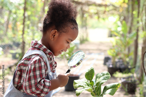 Happy African girl with black curly hair holding magnifying glass for exploring garden form, kid observes nature with magnifying glasses, child education of nature and plant