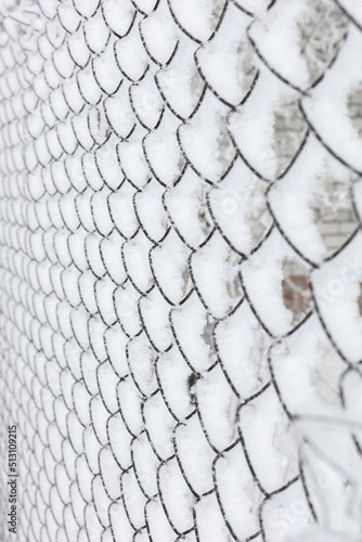 Vertical close-up of thin steel old netting covered with snow encircling some area with denied access. Protests with people going to rallies. Exile to Siberia. Imprisonment.