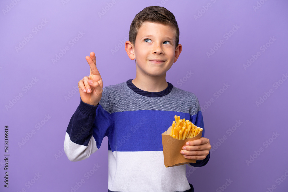 Little boy holding fried chips isolated on purple background with fingers crossing and wishing the best Little boy holding fried chips isolated on purple background with fingers crossing and wishing the best