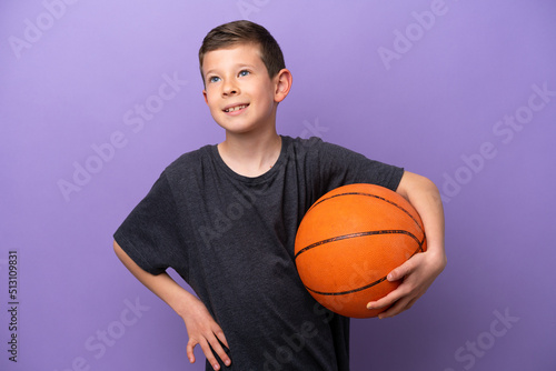 Little boy playing basketball isolated on purple background posing with arms at hip and smiling