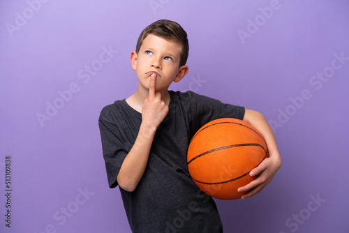 Little boy playing basketball isolated on purple background having doubts while looking up