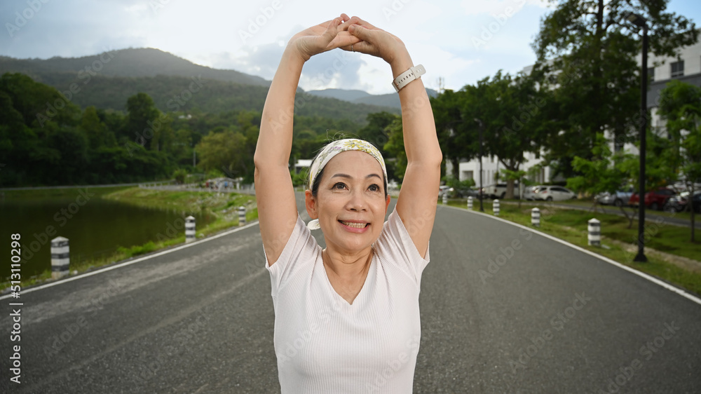 Smiling middle aged woman stretching muscle before workout session at the park in early morning. Healthy lifestyle, fitness and sport concept concept