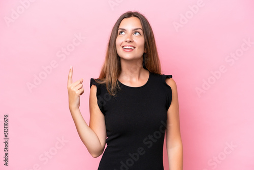 Young caucasian woman isolated on pink background pointing up and surprised © luismolinero