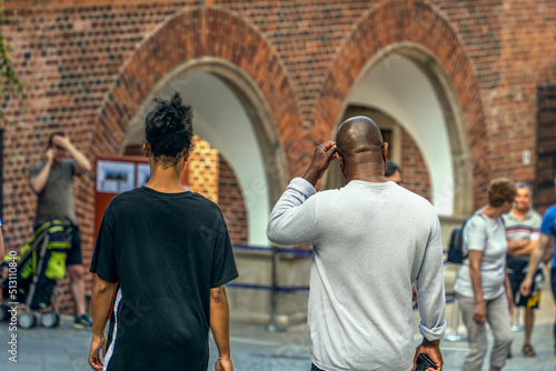 Young ethnic couple on the street of a European city, visiting historical places near the locals, dark-skinned elegant woman in a black t-shirt next to a dark-skinned man with a phone in his hand