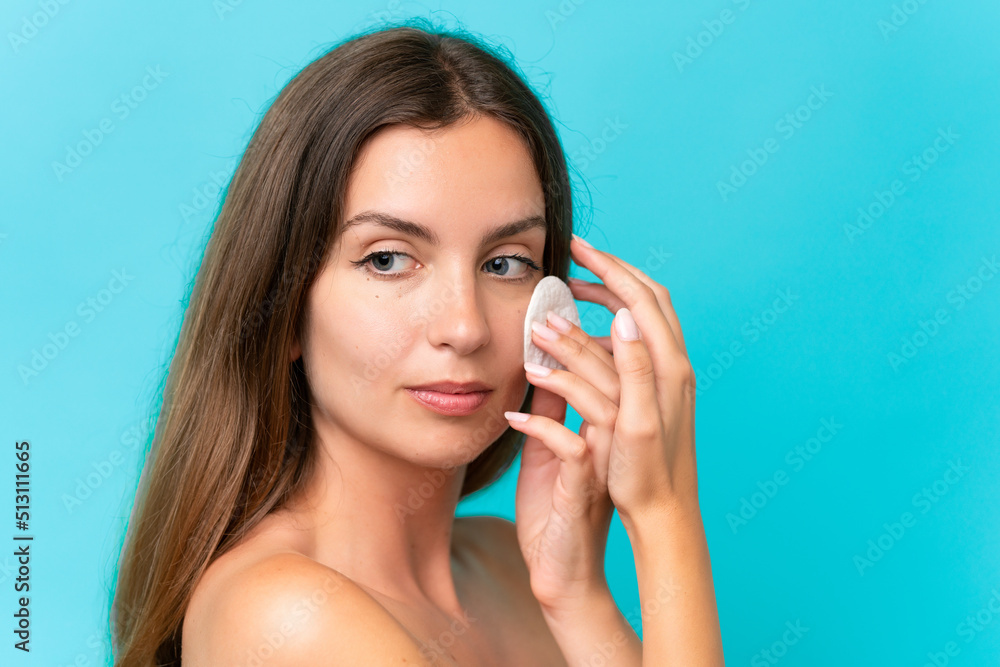 Young caucasian woman isolated on blue background with cotton pad for removing makeup from her face Young caucasian woman isolated on blue background with cotton pad for removing makeup from her face