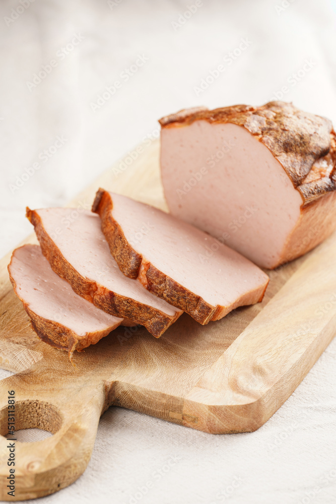 Traditional oven baked bavarian meal leberkäse sliced - meat dish made of corned beef, pork and bacon, finely ground and bakes as a bread loaf, on wooden board on beige colored table cloth Traditional oven baked bavarian meal leberkäse sliced - meat dish made of corned beef, pork and bacon, finely ground and bakes as a bread loaf, on wooden board on beige colored table cloth