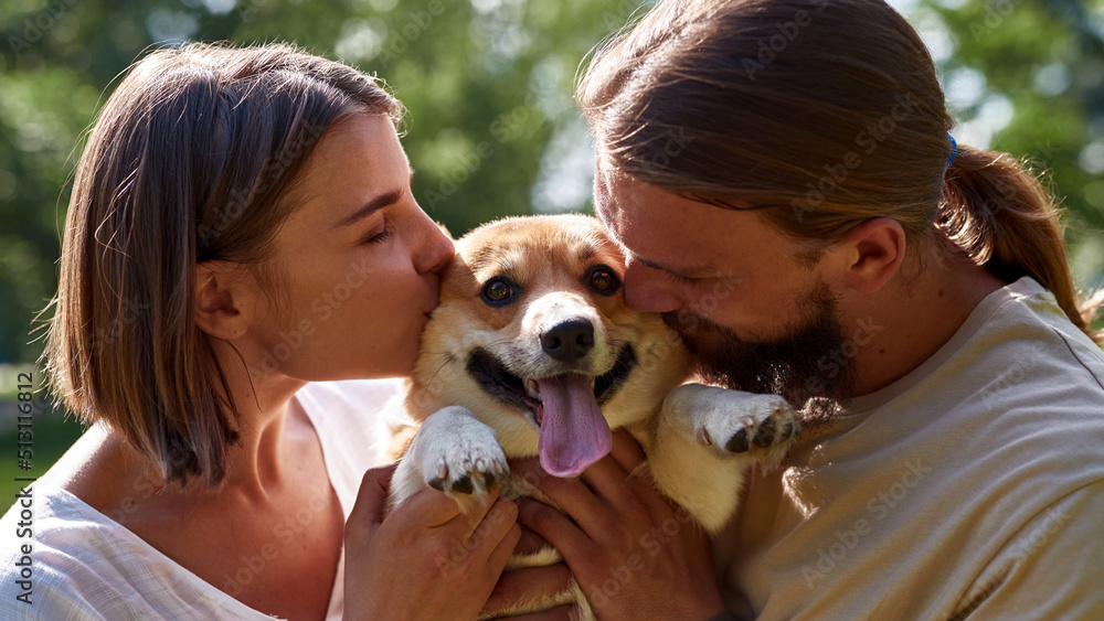 Young caucasian couple kissing Corgi dog in park Young caucasian couple kissing Corgi dog in park