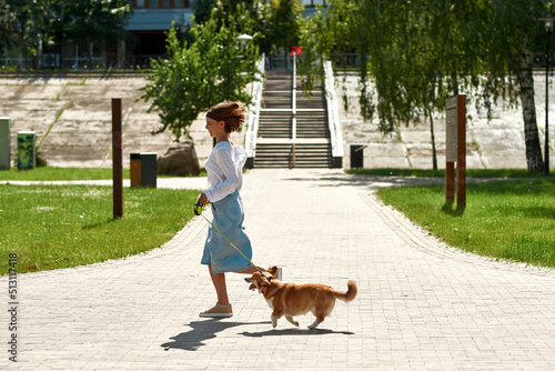 Girl running with Corgi dog on sidewalk in park