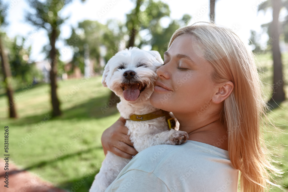 Smiling girl hugging Maltese dog in blurred park Smiling girl hugging Maltese dog in blurred park