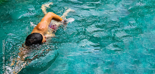 Man swimming freestyle in the pool. Triathlon fitness athlete swimming training. Swimmer person floating in turquoise water banner panorama. Sports and fitness cardio exercises. Panorama banner.