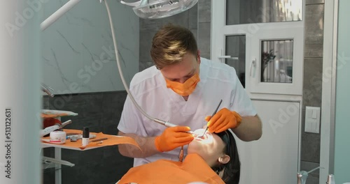 dental hygiene, dentist man in mask and sterile gloves doing teeth cleaning for patient who with dilator in mouth lies in chair in dental clinic photo