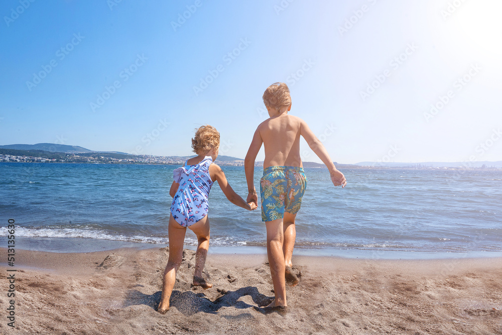 Happy children running and playing together in the sea in summer. Friends holding hands and enjoying summer holidays together.