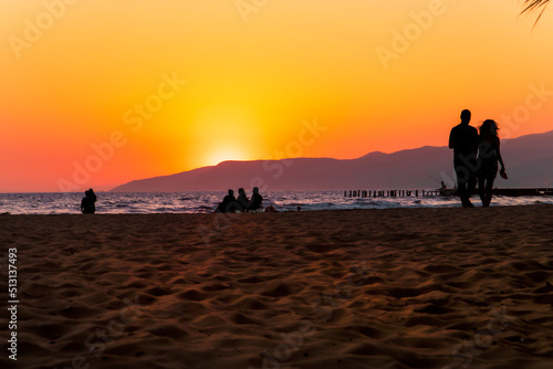 Sunset near coastal beach, people are enjoying the view, fishing, sitting and a couple walking on the sands