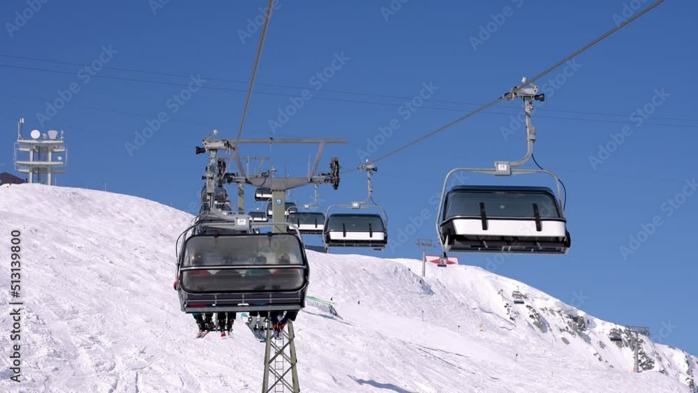 Ski lift moving over snowy landscape in Austrian Alps. Chairlift against clear blue sky. Tourists enjoying winter in the ski resort in Alps. Ski lift moving over snowy landscape in Austrian Alps. Chairlift against clear blue sky. Tourists enjoying winter in the ski resort in Alps.