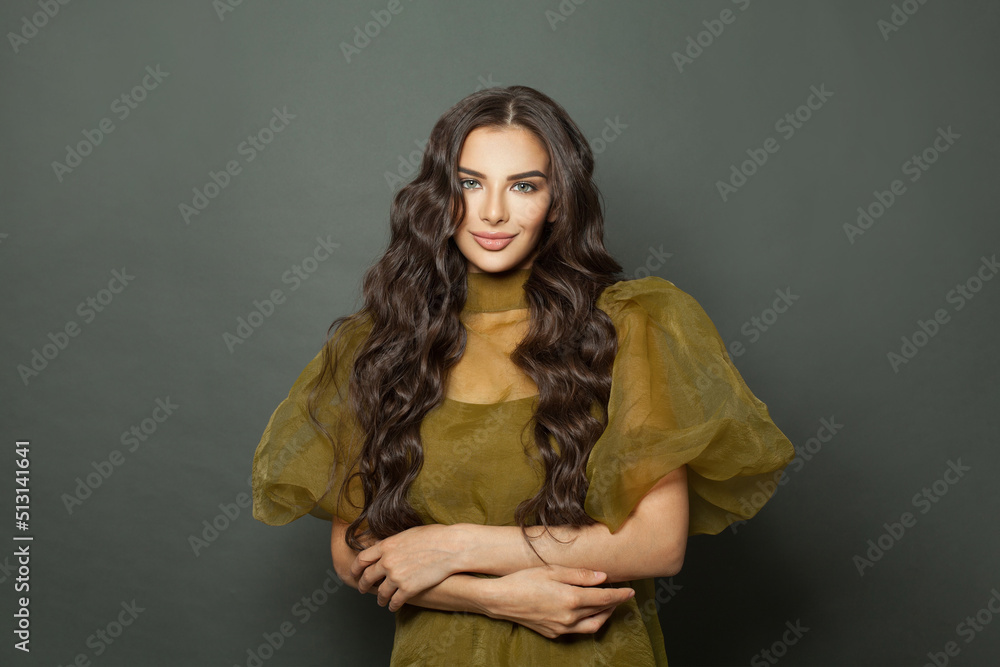 Smiling brunette woman with long wavy hairstyle wearing green dress on black studio background. Fashion and hair care concept. Smiling brunette woman with long wavy hairstyle wearing green dress on black studio background. Fashion and hair care concept.