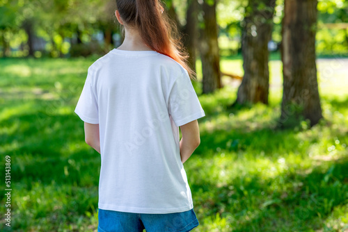 A teenage girl in a white T-shirt with her back to the camera, on a walk in a city park close-up. Solid color clothing with space for text or pattern.