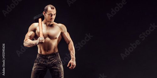Muscular man with great anatomy posing on a black background with a big hummer in his hands
