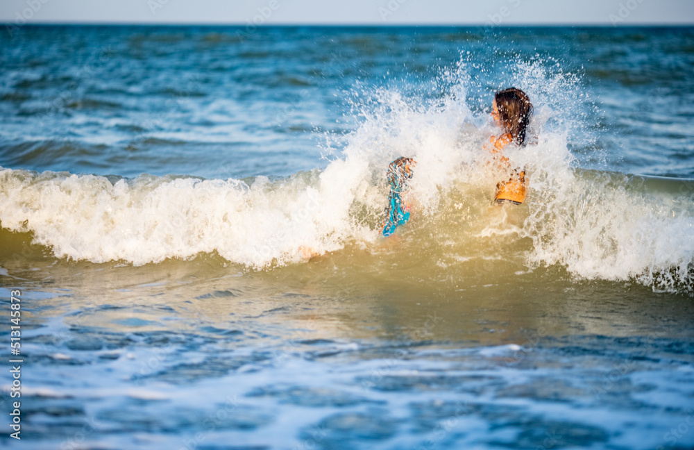 Two sisters in summer swimsuits splash in the sea waves aground on a sunny evening of vacation