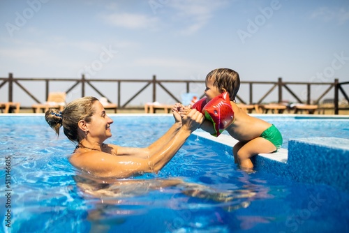 Mom plays with her son with oversleeves in the pool in summer photo