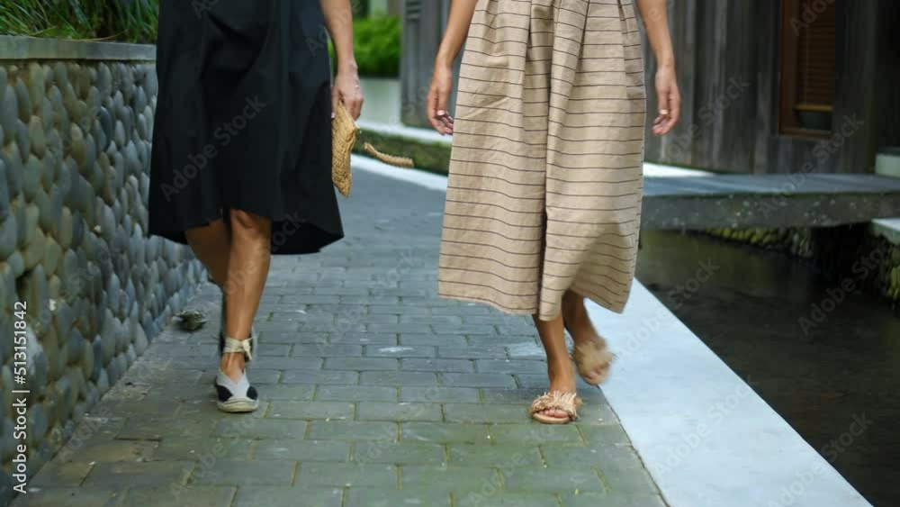 The European ladies walking in white long dresses down a narrow street with a small river The European ladies walking in white long dresses down a narrow street with a small river