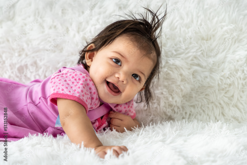 Little Asian baby girl crawling on carpet at home. Newborn child relaxing in bed. Nursery for young children. Looking at camera.