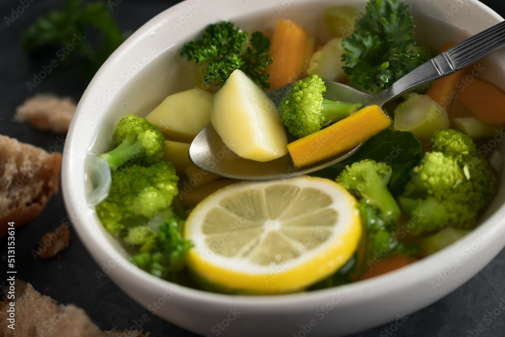 Vegetarian vegetable soup with carrots, broccoli and parsley in a light bowl on a metal tray on a wooden table Vegetarian vegetable soup with carrots, broccoli and parsley in a light bowl on a metal tray on a wooden table