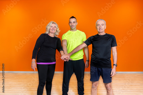 senior fit people celebrating end of the training session together with a low five with a personal trainer. elderly mature person team up inside gym after workout. train and healthy sport concept