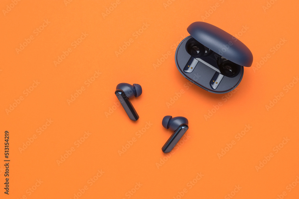 Blue wireless headphones with an open case on an orange background. A popular wireless gadget. Blue wireless headphones with an open case on an orange background. A popular wireless gadget.