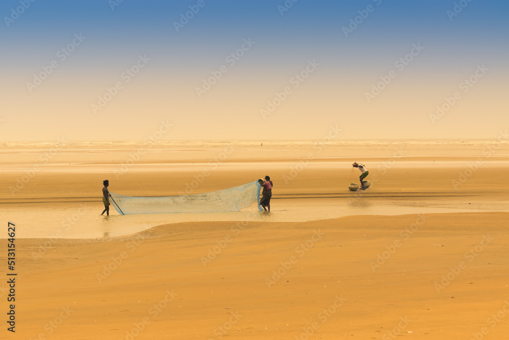 TAJPUR, WEST BENGAL, INDIA - JUNE 22ND, 2014 : A fisherman catching fish with his wife and son with fishing net at seashore of Bay of Bengal. Fishing is means of livelihood for many people at Tajpur.