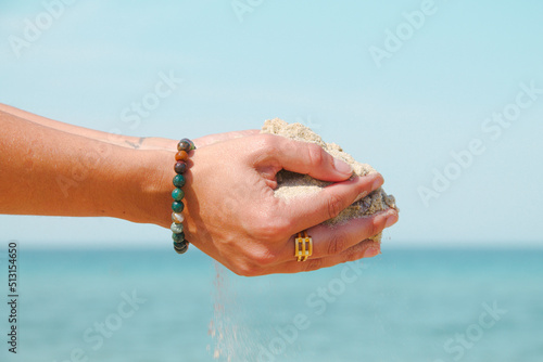 Mains d'une personne portant du sable fin face à la mer.