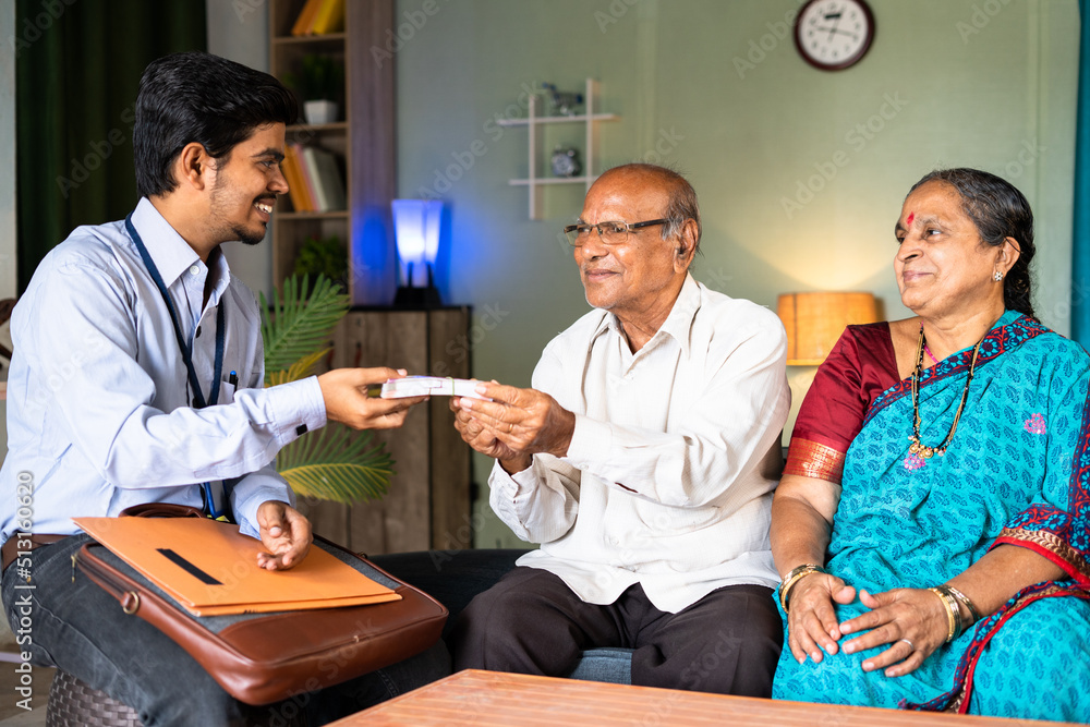 Obraz premium Happy smiling senior couple receiving stack of money from bank officer or insurer at home - concept of insurance claim and home banking support