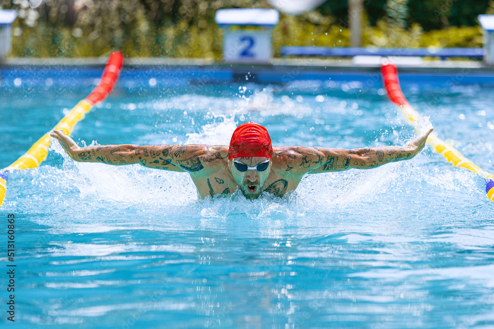One athlete, male professional swimmer in goggles and red swimming cap swimming at public pool, at open-air. Sport, power, energy, style, hobby concept.