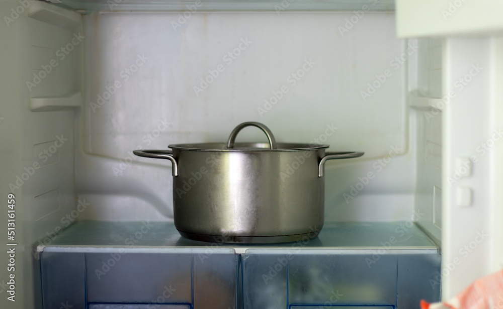 Freezer open pot close-up. Saucepan in an open refrigerator. The refrigerator inside is almost empty due to the economic crisis. Open refrigerator shelves with various cooked food. Freezer open pot close-up. Saucepan in an open refrigerator. The refrigerator inside is almost empty due to the economic crisis. Open refrigerator shelves with various cooked food.