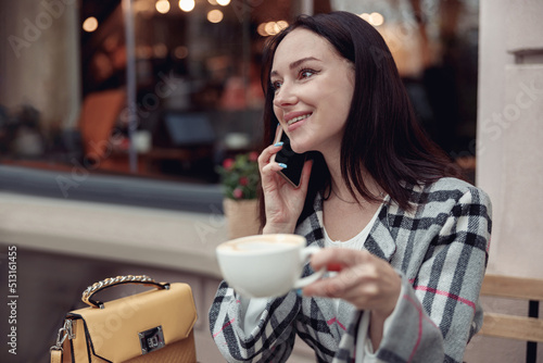 Beautiful young woman talking on mobile phone and drinking cappuccino. Conversation.  photo