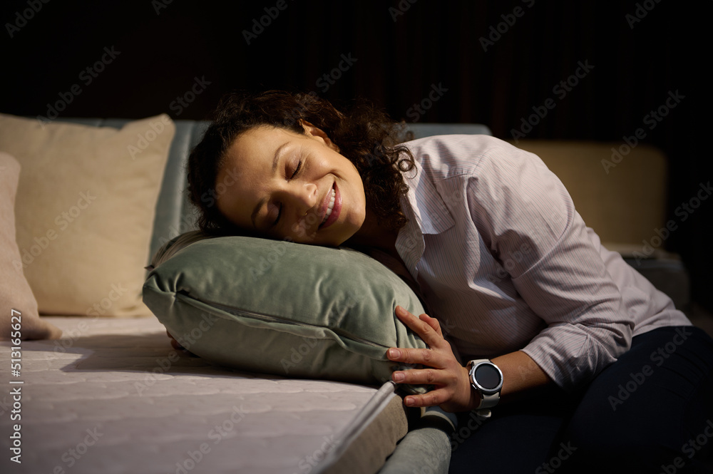 Fototapeta premium Beautiful relaxed Hispanic woman smiles toothy smile while putting her head on a green velour cushion sitting near a sofa bed with orthopedic mattress