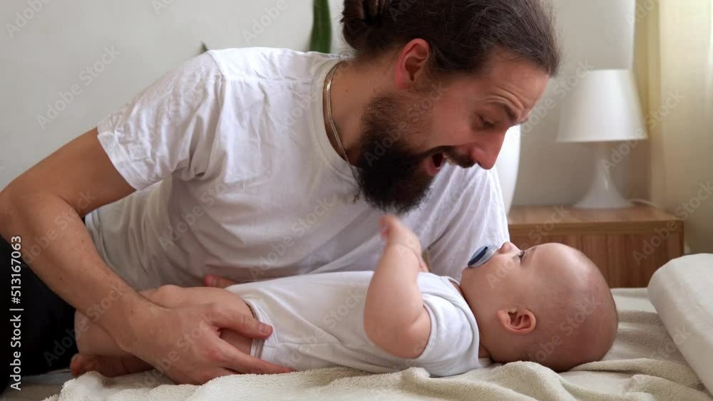 Authentic Bearded Long-haired Young Neo Father And Newborn Baby Looking Each Other Smiling On Bed. Dad Laying With Infant Child. Children, Parenthood, Childhood, Life, Love, Fatherhood, Family Concept Authentic Bearded Long-haired Young Neo Father And Newborn Baby Looking Each Other Smiling On Bed. Dad Laying With Infant Child. Children, Parenthood, Childhood, Life, Love, Fatherhood, Family Concept