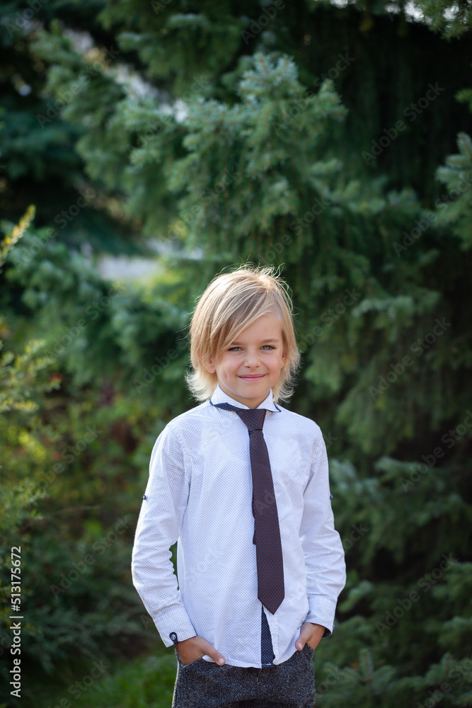 Outdoor portrait of Fashionable Schoolboy with school uniform, blonde boy with long hair looking at a camera Outdoor portrait of Fashionable Schoolboy with school uniform, blonde boy with long hair looking at a camera