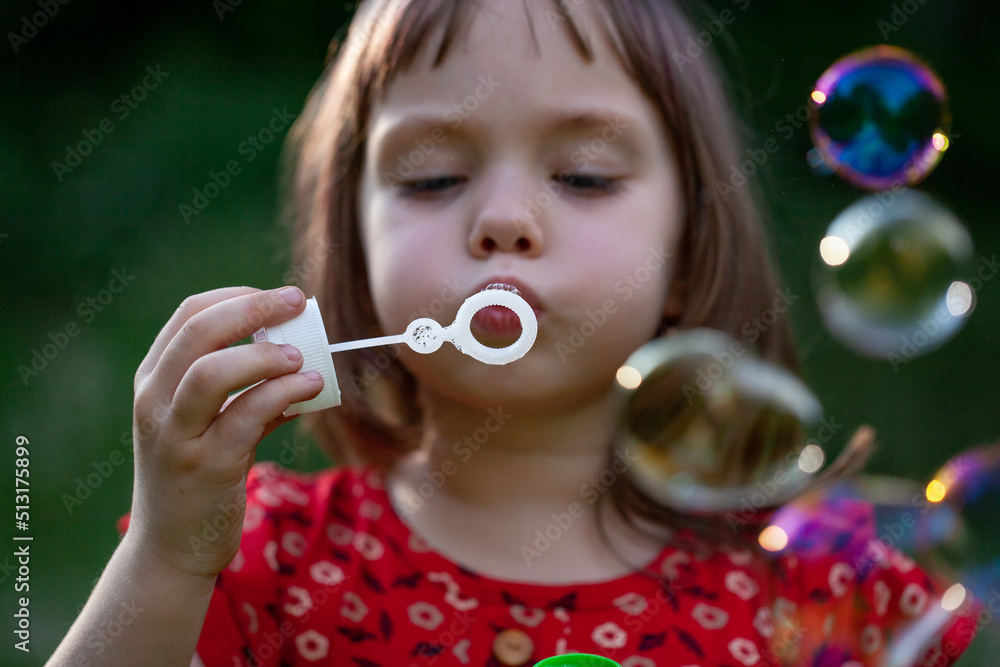 Little child girl in red dress blowing soap bubbles on a summer day at green nature background. Little child girl in red dress blowing soap bubbles on a summer day at green nature background.