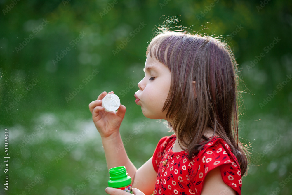 Little child girl in red dress blowing soap bubbles on a summer day at green nature background. Little child girl in red dress blowing soap bubbles on a summer day at green nature background.