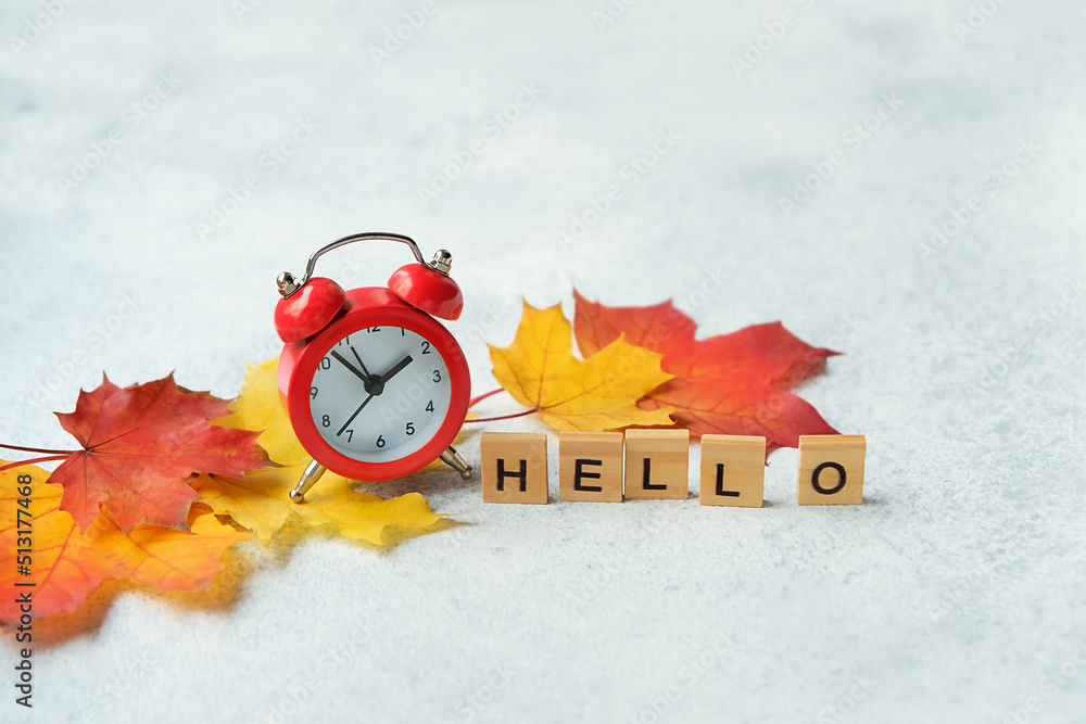 alarm clock, word "hello" of wooden letters and autumn maple leaves close up on abstract grey background. autumn beginning, fall season concept. - obrazy, fototapety, plakaty 