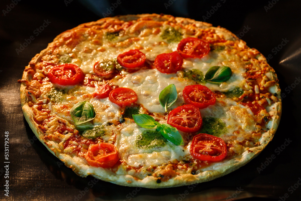 Vegetarian crusty pizza with mozzarella, cherry tomatoes, pesto sauce and basil leaves cook in oven Vegetarian crusty pizza with mozzarella, cherry tomatoes, pesto sauce and basil leaves cook in oven