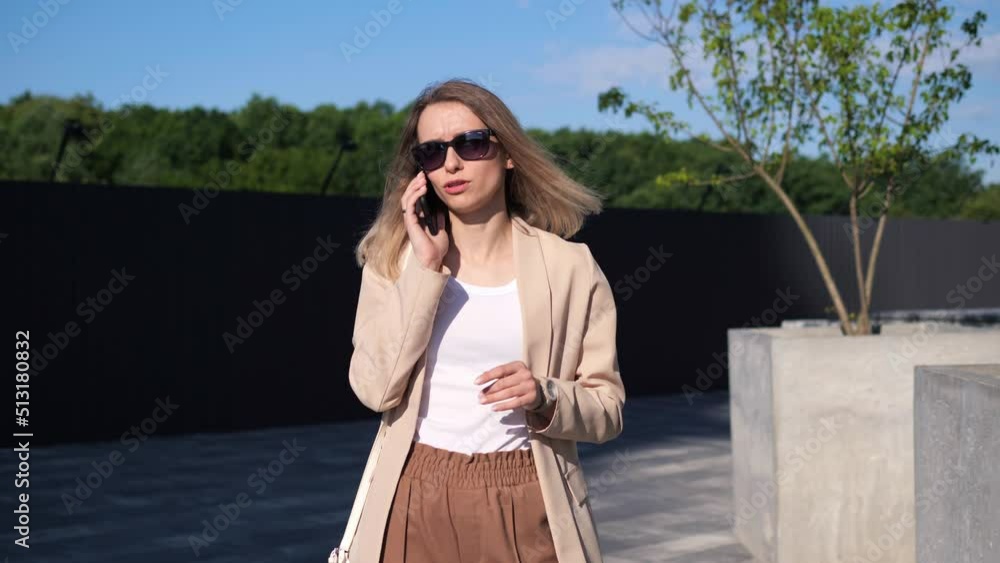 Successful pushful business woman speaking on mobile phone in park area. Businesswoman stands outdoors talking by mobile phone answering business call. Female professional having phone conversation. Successful pushful business woman speaking on mobile phone in park area. Businesswoman stands outdoors talking by mobile phone answering business call. Female professional having phone conversation.